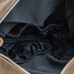 May include: The inside of a brown leather bag with a black satin lining. The lining has a gathered elastic edge.