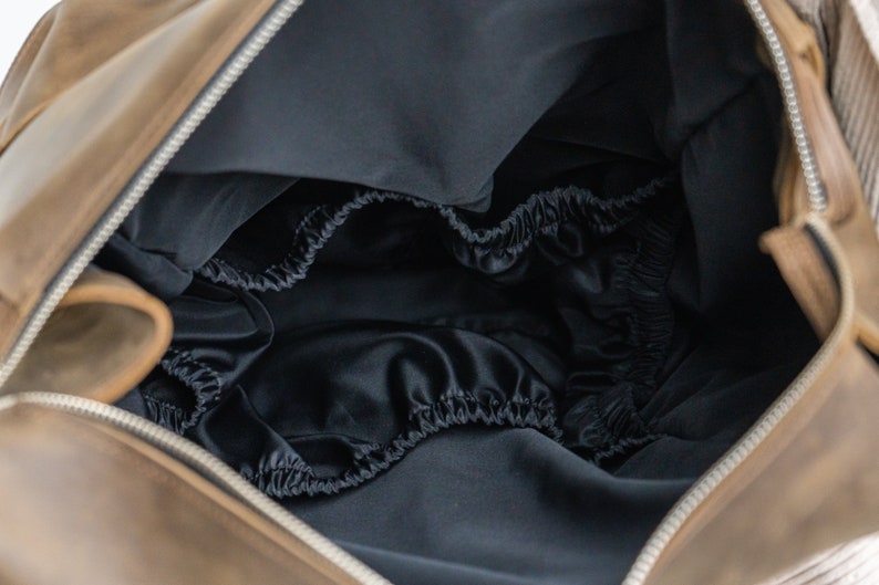 May include: The inside of a brown leather bag with a black satin lining. The lining has a gathered elastic edge.