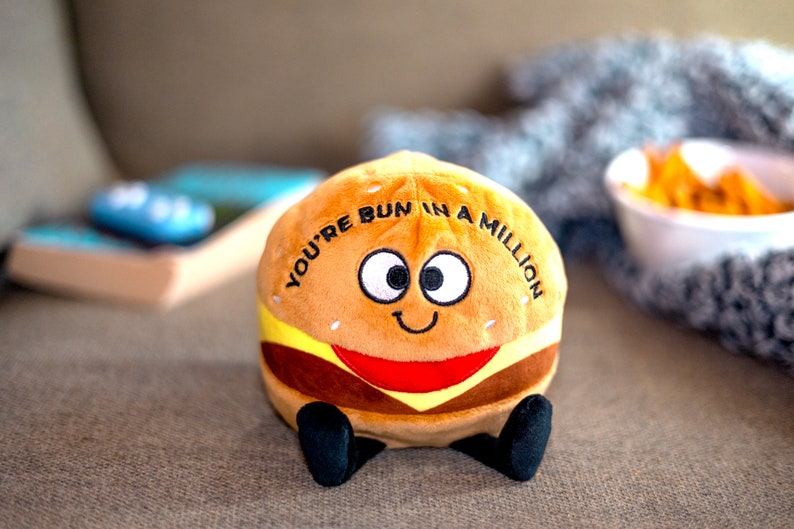 May include: A plush toy shaped like a hamburger with a smiling face and the text "You're bun in a million".