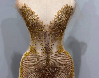 Puede incluir: Una aplicación de pedrería dorada para ropa. La aplicación tiene forma de mariposa y un diseño delicado e intrincado.