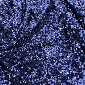 Puede incluir: Un primer plano de una tela azul con lentejuelas. Las lentejuelas son pequeñas y redondas, y están dispuestas en un patrón aleatorio. La tela es suave y brillante.