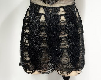 May include: A black beaded skirt with a layered, scalloped design. The skirt is made of small, black beads that are sewn together to create a flowing, elegant look.