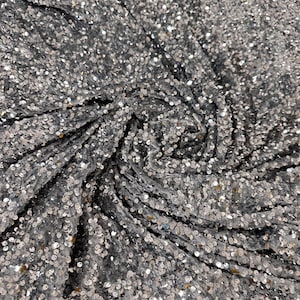 May include: A close-up of a silver sequined fabric. The sequins are small and round, and they are arranged in a random pattern. The fabric is soft and shimmery.