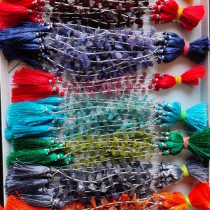 Op de afbeelding: Een verzameling kralenkettingen met kleurrijke kwasten. De kettingen bevatten verschillende edelsteen kralen in tinten geel, rood, blauw, roze, groen en oranje. Elke ketting heeft een bijpassende kwast, wat een levendige weergave creëert.