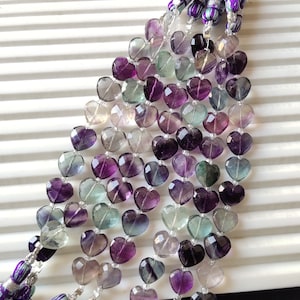 May include: A strand of heart-shaped beads in shades of purple, green, and clear. The beads are strung on a silver wire and have a tassel at each end.