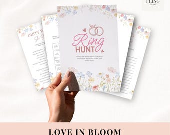 Puede incluir: Una mano sostiene una pila de tarjetas de juego blancas con detalles florales. La tarjeta central dice "Ring Hunt" en escritura rosa, con un gráfico de anillos. La parte inferior de la imagen dice "Love in Bloom 50 Editable Hen Do Games."