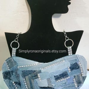 May include: A denim necklace with rhinestones and a silver chain. The necklace is in the shape of a heart and is made of different shades of blue denim. The necklace is displayed on a black mannequin bust. The text "Simplyronaoriginals.etsy.com" is visible on the image.