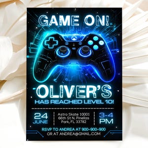Puede incluir: Una tarjeta de invitación rectangular con fondo negro y un gráfico de mando de videojuego azul brillante. El texto dice: GAME ON! OLIVER'S HAS REACHED LEVEL 10! 24 JUNE, Astro Skate 10001 66th St N. Pinellas Park, FL 33782, 3-4 PM, RSVP TO ANDREA AT 900-900-900 OR AT ANDREA@GMAIL.COM.