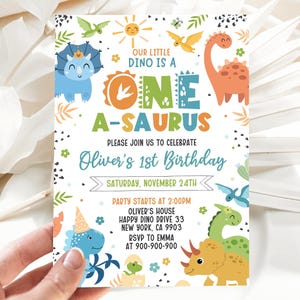 May include: A colorful dinosaur-themed first birthday party invitation with a blue, green, and yellow dinosaur, a sun, and the text "Our little dino is a one a-saurus". The invitation also includes the text "Oliver's 1st Birthday" and the date "Saturday, November 24th".