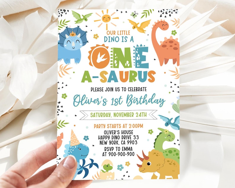 May include: A colorful dinosaur-themed first birthday party invitation with a blue, green, and yellow dinosaur, a sun, and the text "Our little dino is a one a-saurus". The invitation also includes the text "Oliver's 1st Birthday" and the date "Saturday, November 24th".