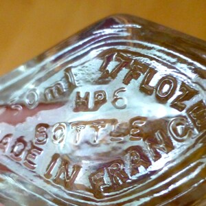 Puede incluir: Una taza de cer&aacute;mica blanca con un asa negra y el texto "But First, Coffee" en negrita negra. La taza se encuentra sobre un fondo borroso, sugiriendo un ambiente acogedor.