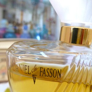 Puede incluir: Un frasco de perfume de vidrio transparente con tapa dorada y el texto "DANIEL de FASSON" en negro. El frasco contiene un l&iacute;quido amarillo y tiene un dise&ntilde;o texturizado y acanalado en los lados.