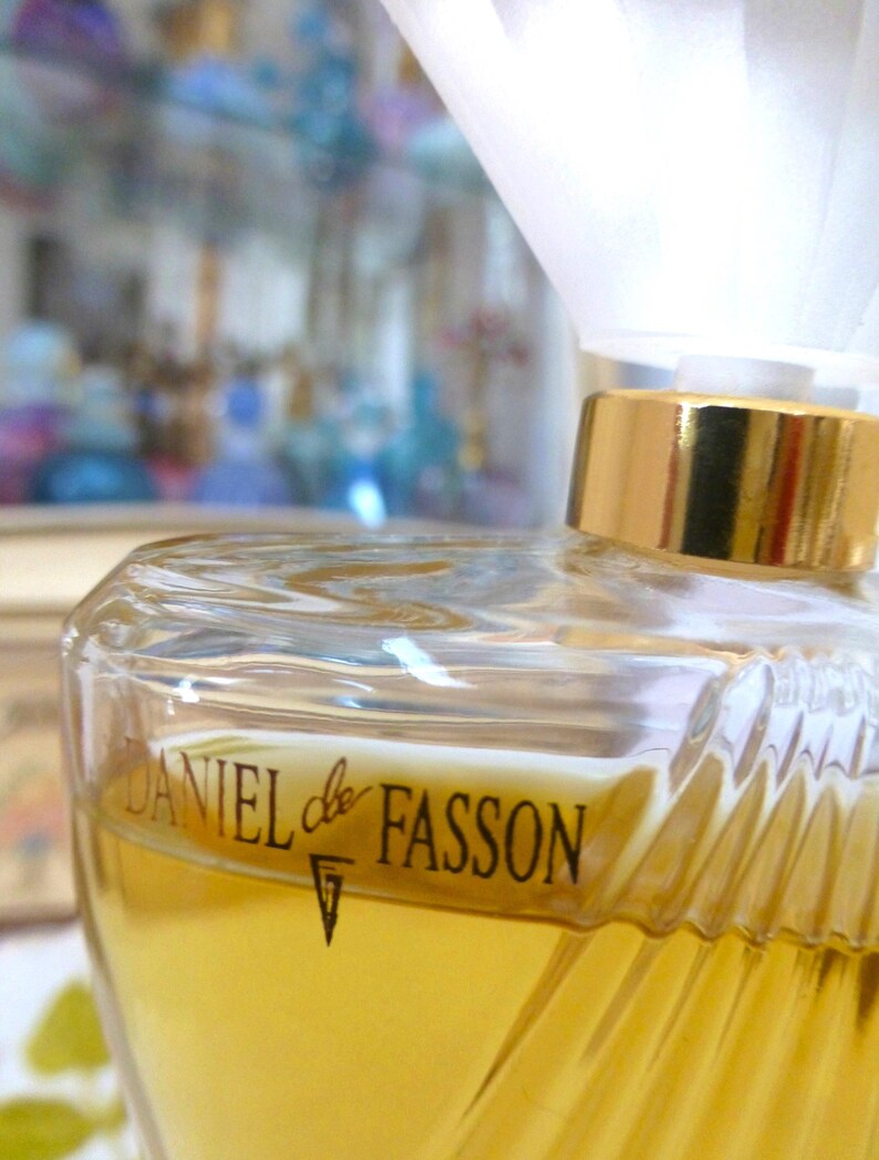 Puede incluir: Un frasco de perfume de vidrio transparente con tapa dorada y el texto "DANIEL de FASSON" en negro. El frasco contiene un l&iacute;quido amarillo y tiene un dise&ntilde;o texturizado y acanalado en los lados.