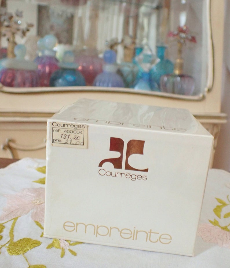 May include: A white box with gold lettering that reads "Courr&egrave;ges" and "empreinte". The box has a small sticker with the text "Courr&egrave;ges", "ref. 460004", "131.20", and "prix. 21.20".