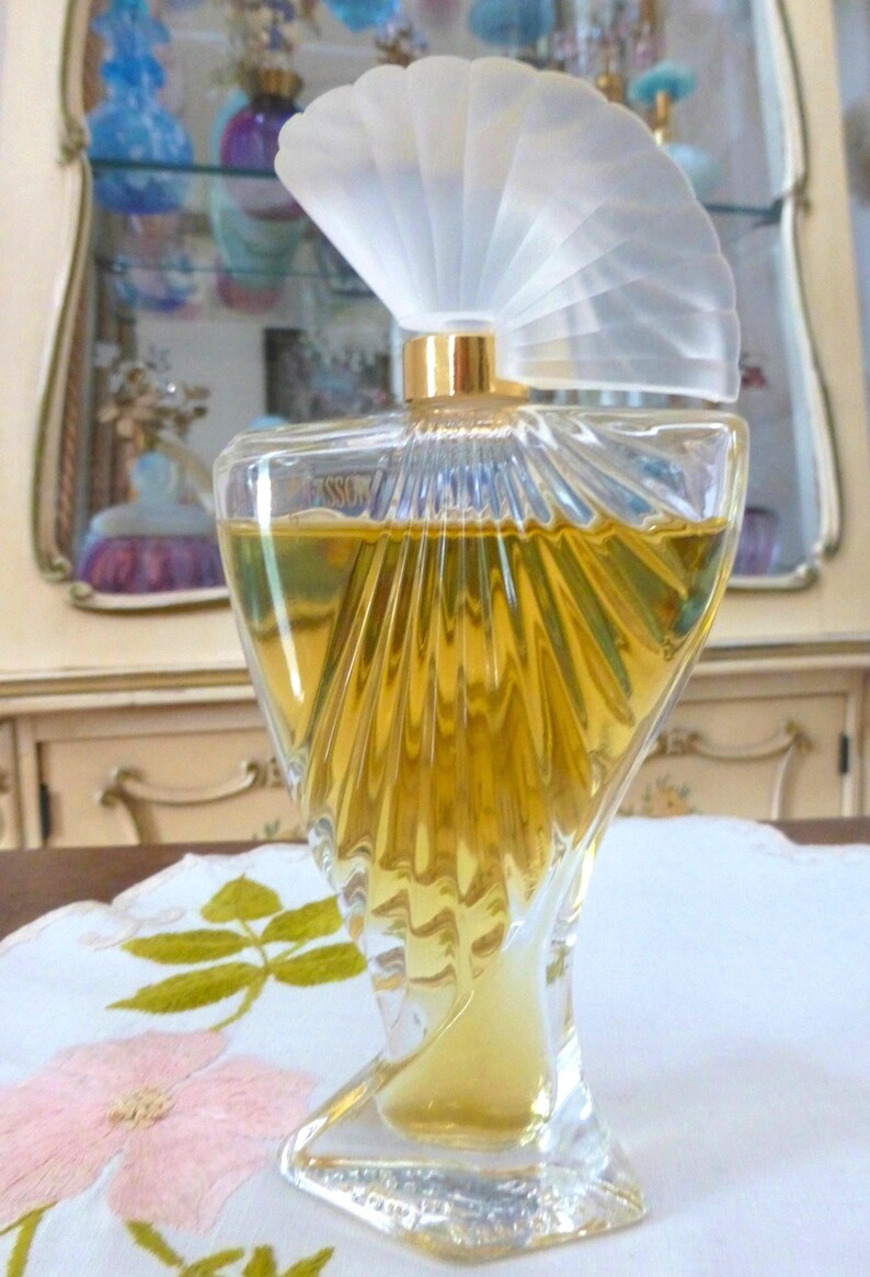 Puede incluir: Una taza de cer&aacute;mica blanca con un asa negra y el texto "But First, Coffee" en negrita negra. La taza est&aacute; llena de un l&iacute;quido oscuro, probablemente caf&eacute;, y se encuentra sobre una superficie de color claro.