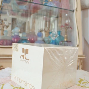 May include: A white box with a clear plastic wrap, featuring the text "Courr&egrave;ges" and "empreinte" in gold lettering. The box is sitting on a white surface with a floral pattern.