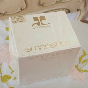 May include: A white box with gold lettering that reads "Courreges" and "empreinte" with a smaller label that reads "1 fl oz - 30 cc".