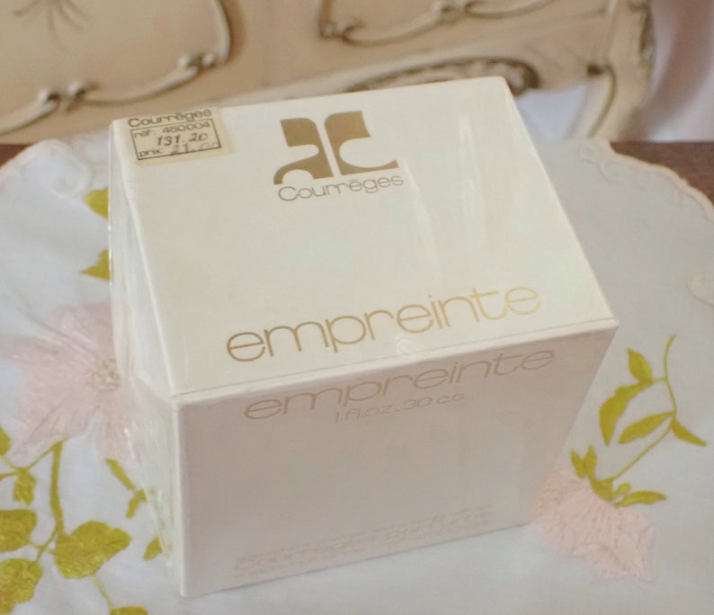 May include: A white box with gold lettering that reads "Courreges" and "empreinte" with a smaller label that reads "1 fl oz - 30 cc".