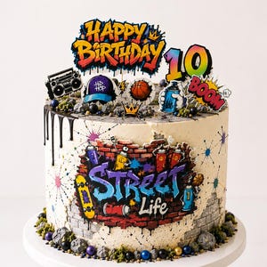 Könnte beinhalten: Ein runder Kuchen mit einem Graffiti-Backsteinwand-Aufdruck, der den Text Street Life, ein Skateboard und Sprühdosen zeigt. Die Tortenaufleger umfassen Happy Birthday, die Zahl 10, einen Ghettoblaster, einen Basketball und eine blaue Sprühdose.