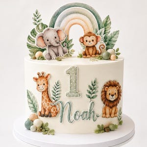 Könnte beinhalten: Eine weiß glasierte Torte, verziert mit Aquarell-Ausschnitten von Dschungeltieren wie Giraffe, Elefant, Affe und Löwe. Die Torte hat einen Regenbogen-Aufsatz, grüne Blätter sowie den Schriftzug "1" und "Noah" in einer hellgrünen Schrift.