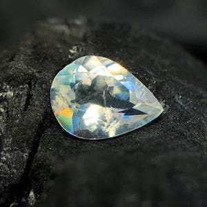 May include: A pear-shaped gemstone with a clear, iridescent finish. The stone is set against a dark background.