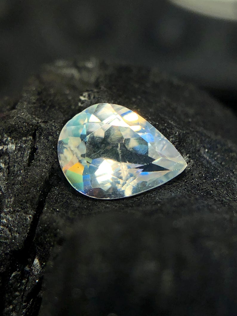 May include: A pear-shaped gemstone with a clear, iridescent finish. The stone is set against a dark background.