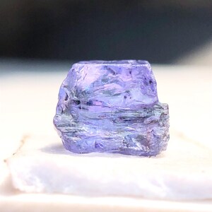 May include: A faceted, purple gemstone with a rough, natural finish. The gemstone is translucent and has a slight shimmer.