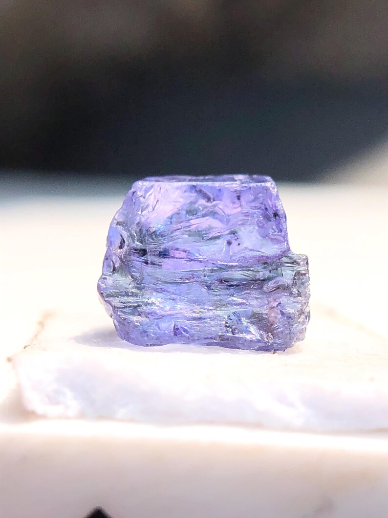 May include: A faceted, purple gemstone with a rough, natural finish. The gemstone is translucent and has a slight shimmer.