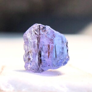May include: A faceted, purple-blue gemstone with a clear, glassy appearance. The gemstone is rough-cut and has a natural, irregular shape.