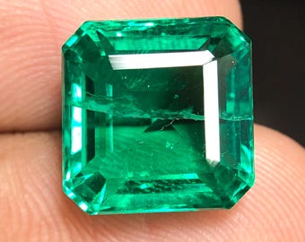 Könnte beinhalten: Ein lebendiger, smaragdgeschliffener grüner Edelstein mit rechteckiger Form. Der Edelstein hat eine tiefe, satte Farbe und eine facettierte Oberfläche, die das Licht reflektiert. Der Edelstein wird zwischen den Fingern gehalten und zeigt seine Klarheit und Brillanz.