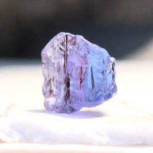 May include: A small, faceted, purple gemstone with a clear, glassy appearance. The gemstone is irregularly shaped and has a slight sheen.