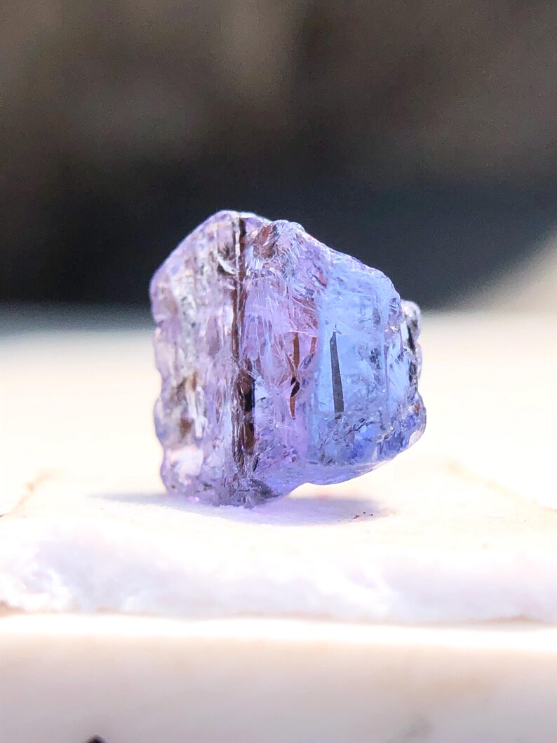 May include: A small, faceted, purple gemstone with a clear, glassy appearance. The gemstone is irregularly shaped and has a slight sheen.