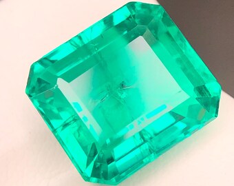 Könnte beinhalten: Ein großer, rechteckiger Smaragd mit leuchtend grüner Farbe. Der Edelstein weist einen Stufenschliff auf, der seine Facetten und innere Klarheit hervorhebt. Der Smaragd ist vor einem weißen und grauen Hintergrund platziert, der seine Farbe und Brillanz unterstreicht.