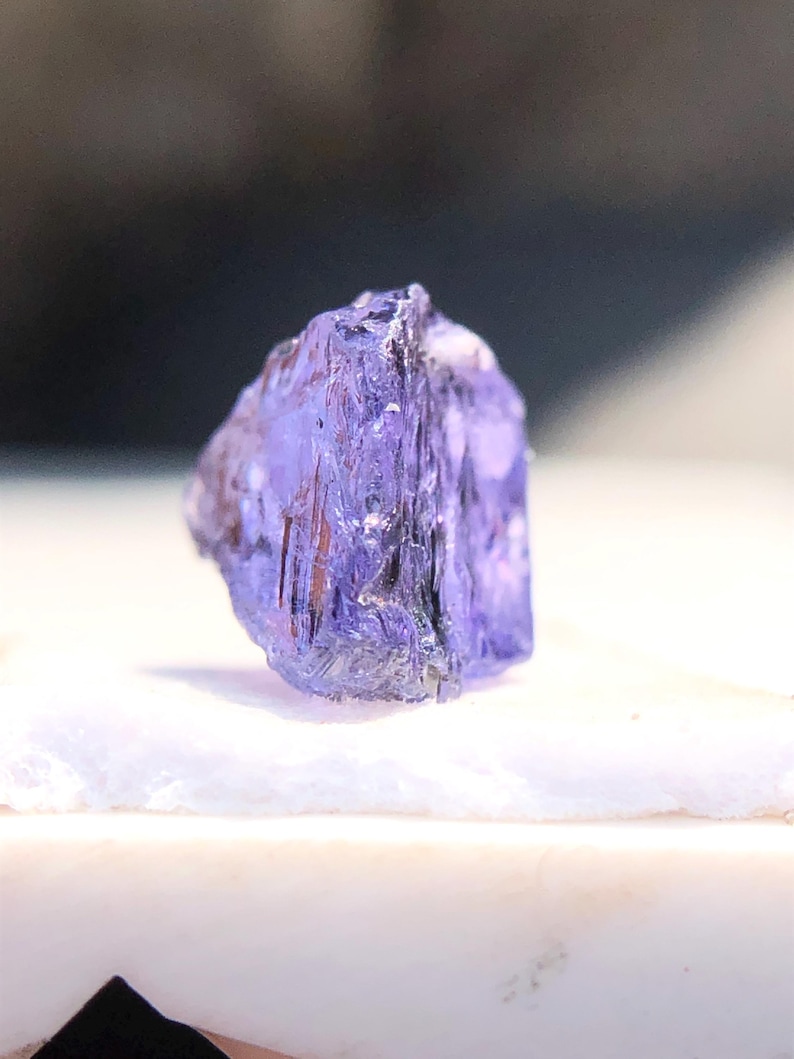 May include: A purple gemstone with a faceted, geometric shape. The crystal is translucent and has a slight sheen.