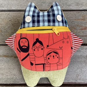 Könnte beinhalten: Ein rotes, gelbes und weißes Stoff-Eulenspielzeug mit einer Reißverschlusstasche. Die Eule hat einen karierten Stoff auf der Rückseite und ein Design mit vier Comicfiguren auf der Vorderseite.