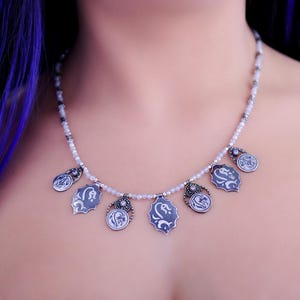 May include: A silver necklace with a white beaded chain and multiple silver charms. Each charm features a floral design with a black and white pattern.