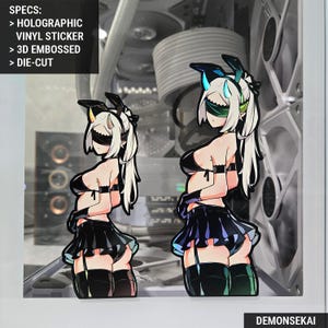 May include: Two holographic vinyl stickers of a female anime character with white hair, a black outfit, and a blindfold. The stickers are 3D embossed and die-cut. Text on the image reads "SPECS: > HOLOGRAPHIC VINYL STICKER > 3D EMBOSSED > DIE-CUT" and "DEMONSEKAI".