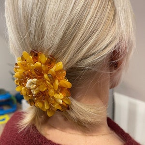 May include: A large amber hair clip with a flower-like design. The clip is made of many small, irregular pieces of amber.