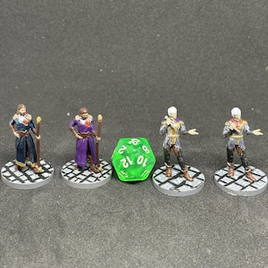 May include: Four miniature fantasy figures in various outfits, standing on circular bases. A large green 12-sided die is in the center. The figures are painted with detail, suggesting a tabletop role-playing game theme.