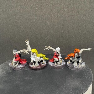 Puede incluir: Cuatro figuras de fantasía en miniatura con pintura detallada. Cada figura tiene una combinación de colores única, incluyendo cabello rojo, amarillo y naranja, y está posada sobre una base circular. Las figuras tienen brazos esqueléticos y están en posición agachada.