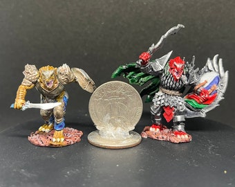 May include: Two painted miniature figurines of fantasy creatures. The first is a lizard-like creature with a sword and shield, painted in gold, brown, and blue. The second is a red-skinned creature with a sword and shield, painted in silver, red, and green. Both figures are standing on a brown base.