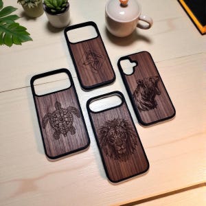 Peut inclure: Quatre coques de téléphone en bois avec des bordures noires, chacune gravée d'un animal différent : un loup, un ours, un lion et une tortue. Les coques ont un fini grain de bois naturel et les motifs animaliers sont finement détaillés.