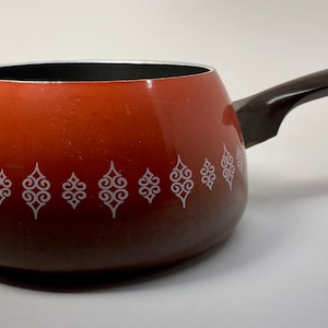 May include: A brown and orange enamel saucepan with a black handle. The saucepan has a white design of repeating swirls around the middle.