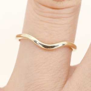 Op de afbeelding: Een eenvoudige gouden ring met een gebogen, golvend ontwerp. De ring wordt aan een vinger gedragen.