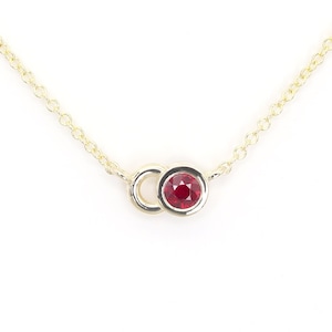 May include: A delicate gold chain necklace with a small red gemstone set in a gold circle pendant.