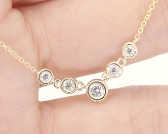 May include: A gold chain necklace with five round clear gemstones. The gemstones are set in a bezel setting and are arranged in a curved line.