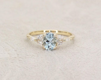 May include: A gold ring with an oval aquamarine gemstone surrounded by smaller diamonds. The ring has a delicate band.