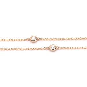 May include: Rose gold chain necklace with two bezel-set diamonds. The diamonds are round and sparkle against the delicate chain. The necklace is displayed against a white background.