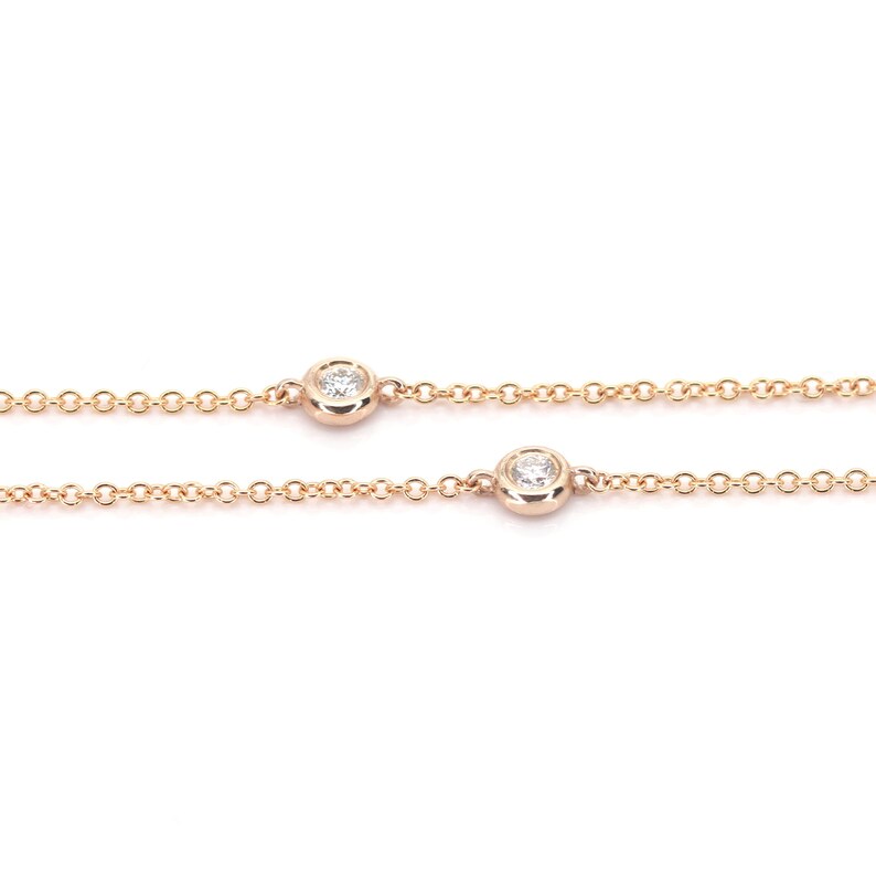 May include: Rose gold chain necklace with two bezel-set diamonds. The diamonds are round and sparkle against the delicate chain. The necklace is displayed against a white background.