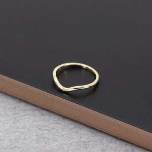 Op de afbeelding: Een eenvoudige gouden ring met een gebogen, v-vormig ontwerp. De ring ligt op een zwart oppervlak.